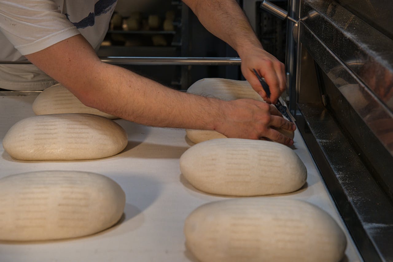 A baker in Berlin shaping artisanal bread loaves on a baking tray at an artisan bakery.